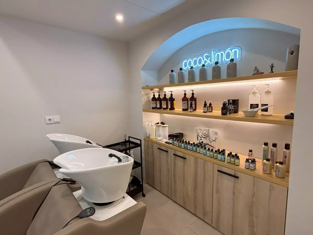 Zona de lavado de pelo de la peluquería con una estantería al fondo repleta de productos de belleza y cuidado
